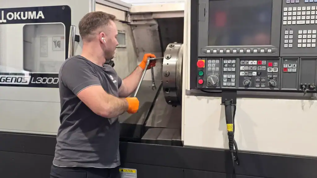 Technician servicing Okuma CNC lathe spindle and control panel in workshop